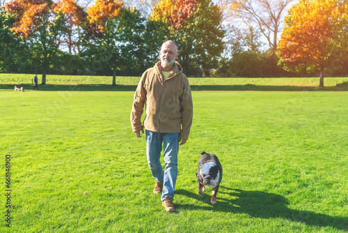 An old man walking with his dog in the park
