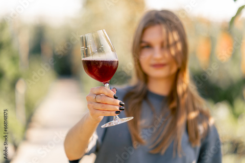 Portrait of a beautiful long-haired girl takes a sip of wine from a glass and hands it to the camera with smile