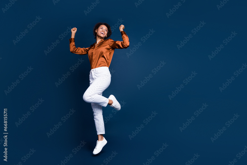 Fototapeta premium Full size photo of attractive young woman jump celebrate win dressed stylish brown silk formalwear isolated on dark blue color background