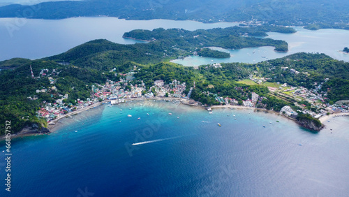 Aerial view of a small town on the shore of a lagoon on a tropical island. Small town, bay, lagoon, boats in the port. Sabang, Puerto Galera, Oriental Mindoro, Philippines. photo