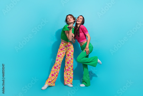 Full body length photo of sending air kiss girlfriends positive coquettish affectionate charming sisters isolated on blue color background
