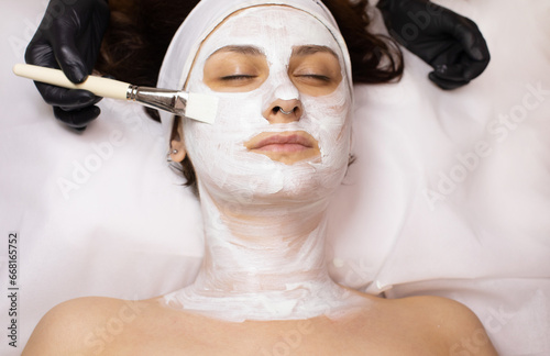 Cosmetologist apply face mask on female client do procedures in spa or saloon. Beautician make facial treatment to woman in medical aesthetic clinic. Skincare, cosmetology and beauty.