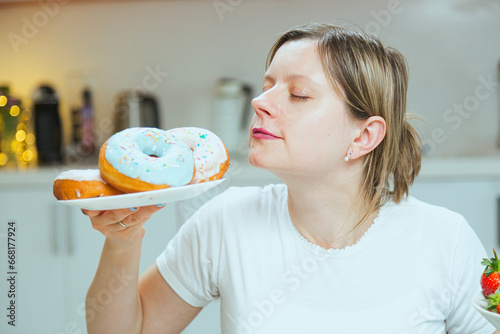 Photo of sugar addicted woman smells freshly baked donuts, impossible to resist eating dessert. Concept of dieting, resistance