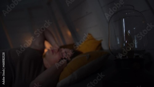 The girl asleep inside a hut wakes up and turns on the light.