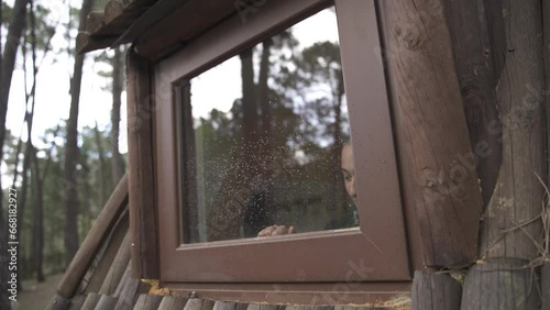 Girl in hat and autumn clothes opens the window of a log cabin during autumn.