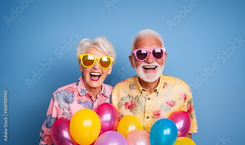 Portrait of a happy elderly couple with sunglasses wearing colorful shirts holding balloons