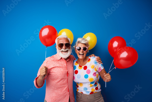 Portrait of a happy elderly couple with sunglasses wearing colorful shirts holding balloons