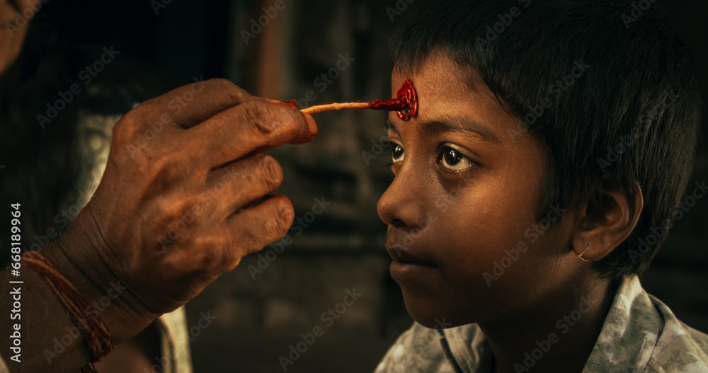 Authentic Footage of Hindu Priest Putting a Tilaka on Male Kid in a Temple. Senior Guru Giving Blessings with a Mark on the Forehead to a Child, Faithful Worshipers in Religious Ceremony - obrazy, fototapety, plakaty 
