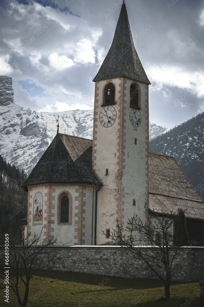 Vertical shot of a historic chapel and clock tower in the Dolomites