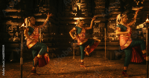 Portrait of Three Expressive Young Indian Dancers Performing Folk Dance Choreography Inside an Ancient Temple. Women in Traditional Clothes Dancing Bharatanatyam in Colourful Sari