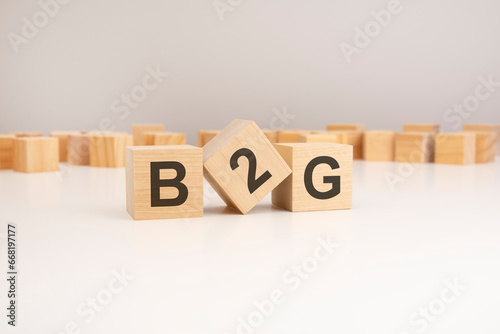 three wooden cubes with B2G symbols on them. white background. in the background there are many wooden blocks of different sizes