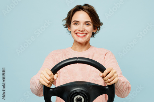 Young smiling happy fun woman wear beige knitted sweater casual clothes hold steering wheel driving car look camera isolated on plain pastel light blue background studio portrait. Lifestyle concept. photo