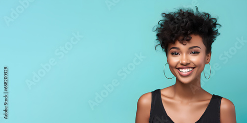 Smimilg young woman with dark skin and short groomed hair isolated on flat blue pastel background with copy space. Model for banner of cosmetic products, beauty salon and dentistry