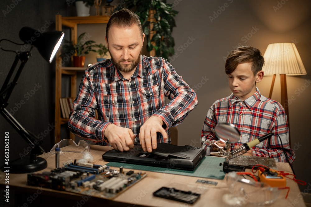 Happy boy and his father sitting together and repairing motherboard using soldering iron. Family together