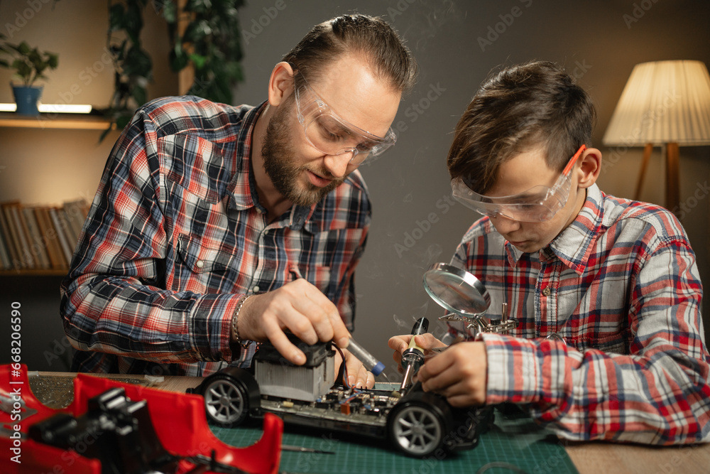 © Andrii Lysenko - Father teaching his son for soldering and repair remote controlled car at home. Man and boy fixing broken toy.