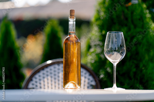 Close-up shot of a glass bottle with wine and a glass stand on the table of a summer terrace of restaurant for tasting