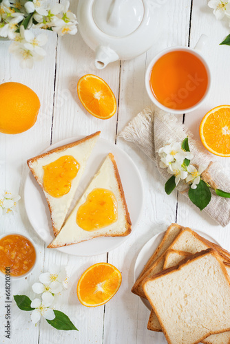 Delicious toast with butter and orange jam and tea on a white wooden background with flowers and fruits. Excellent breakfast.