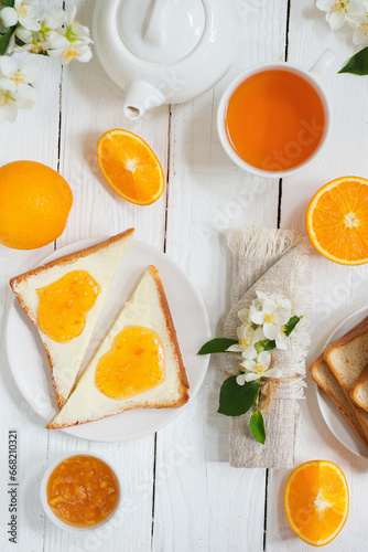 Delicious toast with butter and orange jam and tea on a white wooden background with flowers and fruits.