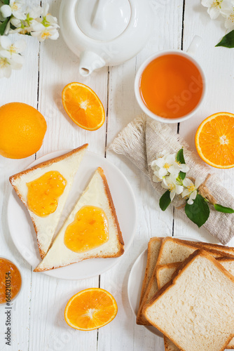 Delicious toast with butter and orange jam and tea on a white wooden background with flowers and fruits.