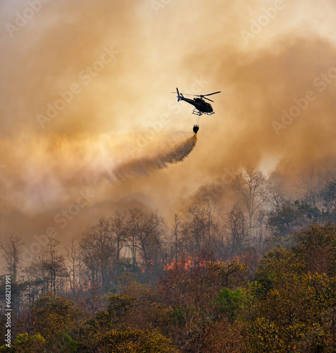 Fire fighting helicopter dropping water onto wildfire because climate change and global warming is a driver of global wildfire trends.