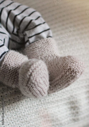 Baby booties tied by hands for a newborn baby. Close-up of children's legs in knitted socks