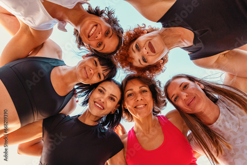 Bottom view of circle group of Caucasian happy smiling women wearing sports clothes looking in camera. Concept of sport and team spirit