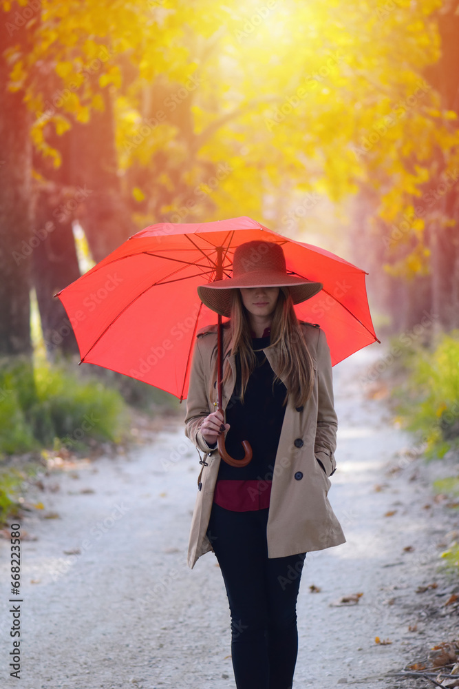 Obraz premium A young woman walks with a red umbrella on a sunny autumn day.