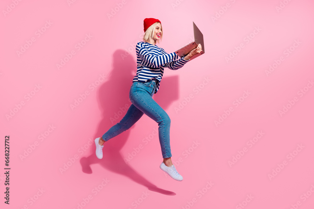 Full length photo of cheerful cute girl dressed striped shirt jumping texting modern device isolated pink color background