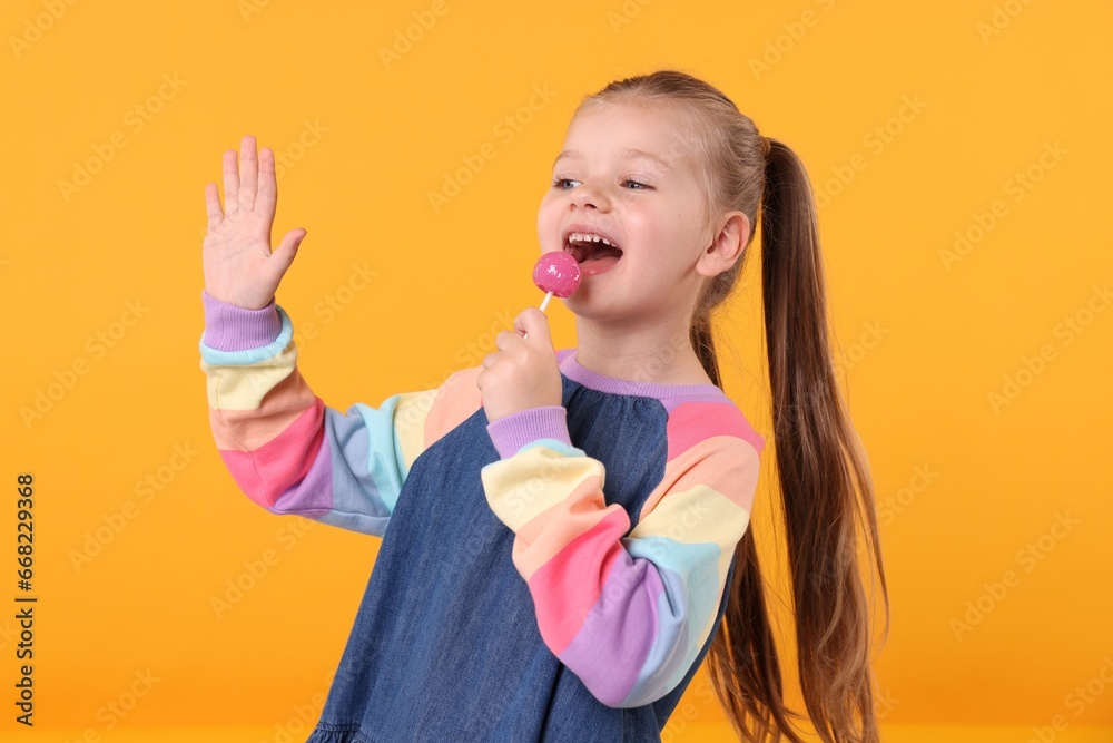 Happy little girl with lollipop on orange background Happy little girl with lollipop on orange background