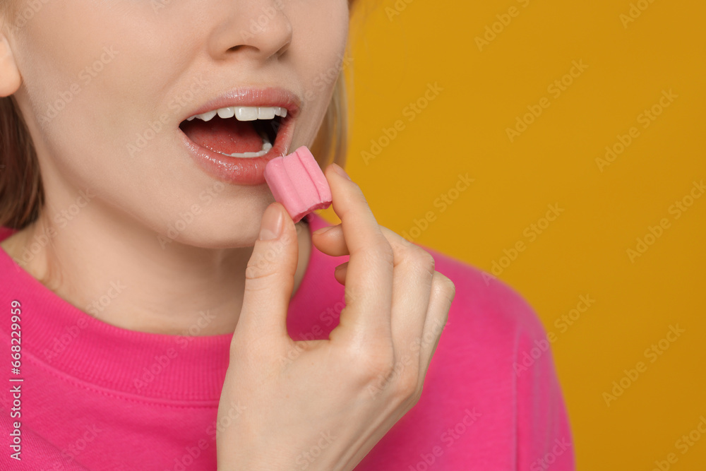 Woman putting bubble gum into mouth on yellow background, closeup. Space for text Woman putting bubble gum into mouth on yellow background, closeup. Space for text