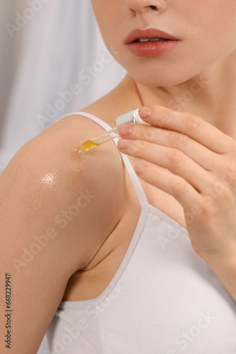 Woman applying essential oil onto shoulder on blurred background  closeup