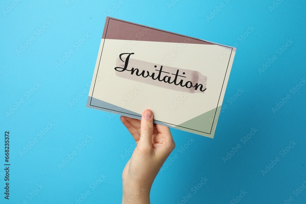 Woman holding beautiful card with word Invitation on light blue background, closeup Woman holding beautiful card with word Invitation on light blue background, closeup