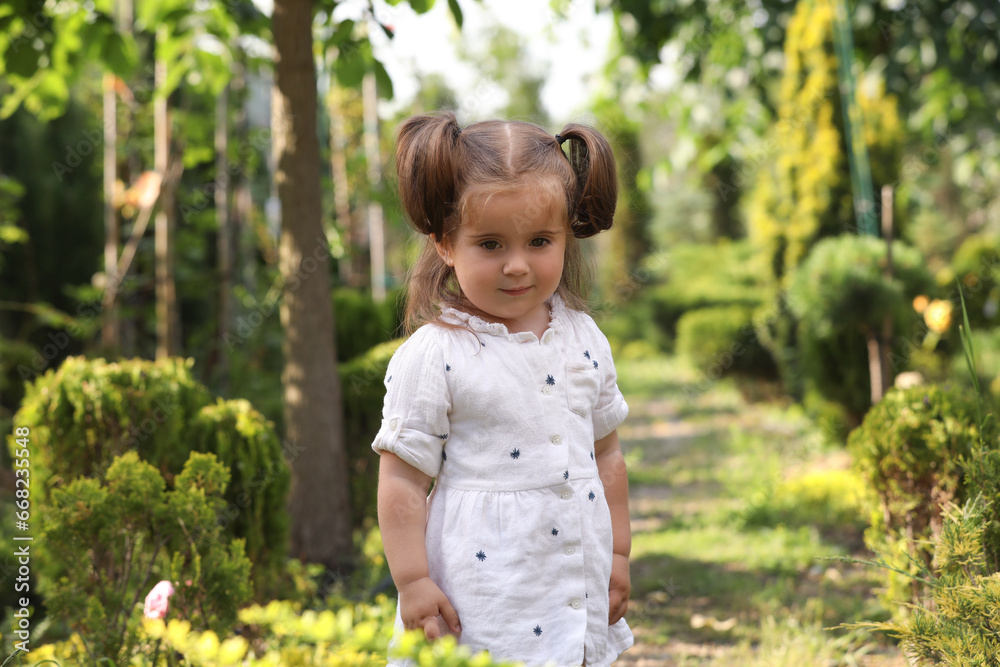 Cute little girl walking near green plants in park Cute little girl walking near green plants in park