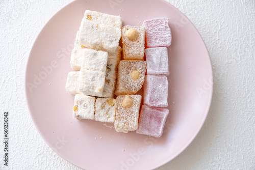 Turkish delights with hazelnuts, pistachios, walnuts, coconut and roses on a pink plate 