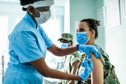 A nurse administers a vaccine to a female soldier in a clinic photo