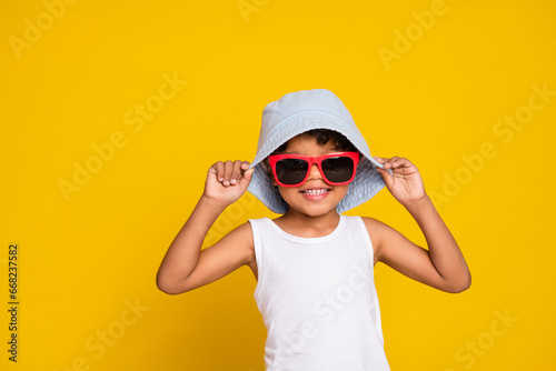 Full length photo of cheerful funky little boy dressed white shirt dark eyewear headwear empty space isolated yellow color background
