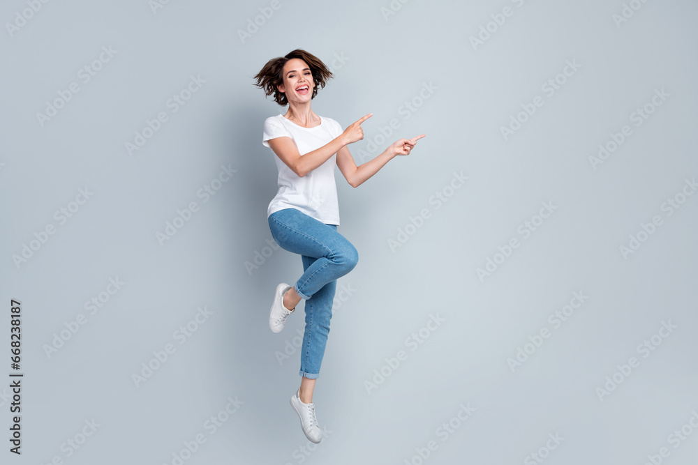 Full body photo of excited energetic lady jumping indicate fingers empty space ad isolated on grey color background