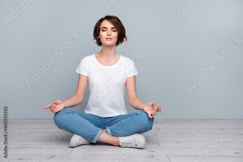 Full size photo of focused relaxed woman dressed white t-shirt sit on floor meditating eyes closed isolated on gray color background