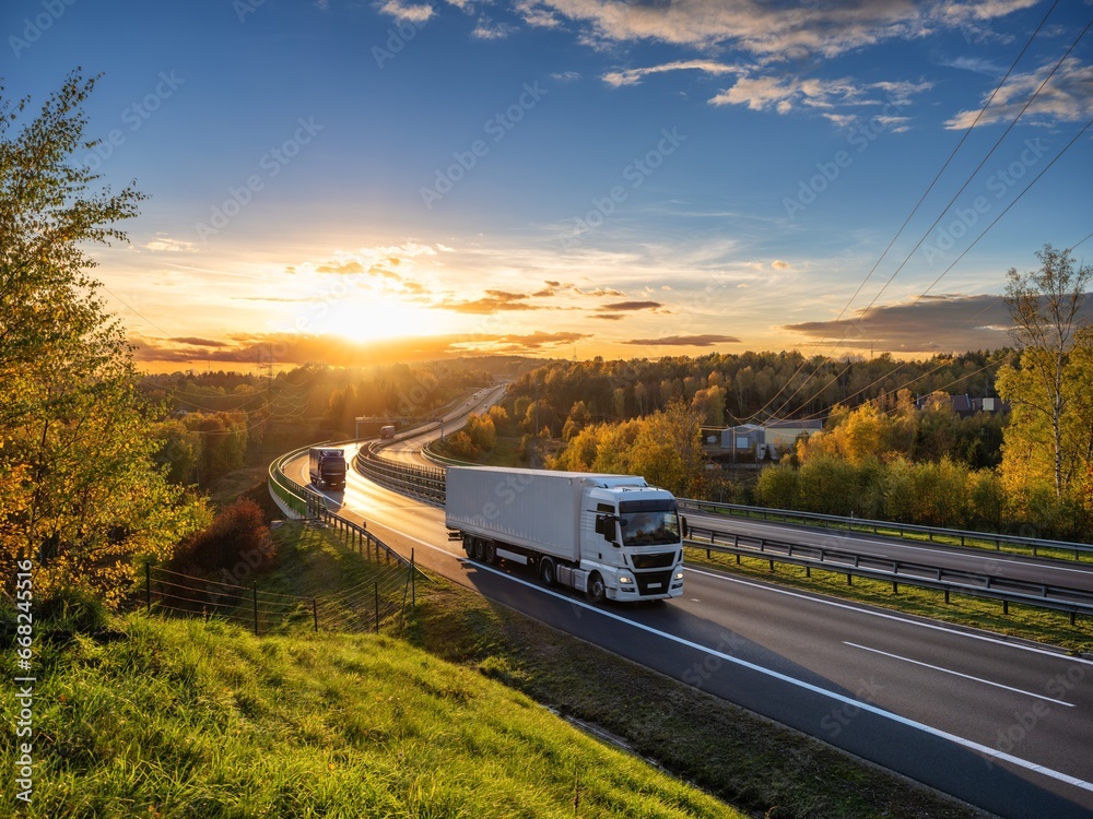 Trucks driving on the highway winding through forested landscape in autumn colors at sunset