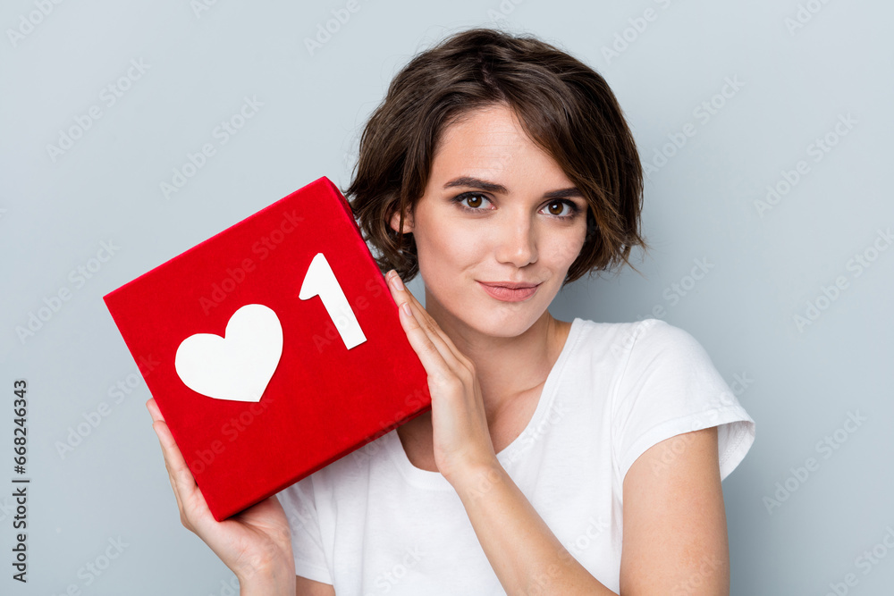 Photo of cheerful gorgeous woman short hairdo dressed white t-shirt holding red box with like icon isolated on gray color background Photo of cheerful gorgeous woman short hairdo dressed white t-shirt holding red box with like icon isolated on gray color background