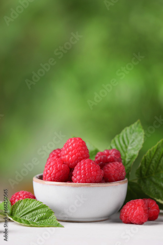 Tasty ripe raspberries and green leaves on white wooden table outdoors, space for text