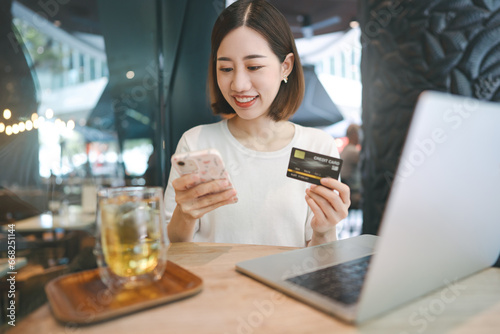 Young adult asian woman using credit card with internet banking mobile app sitting at cafe