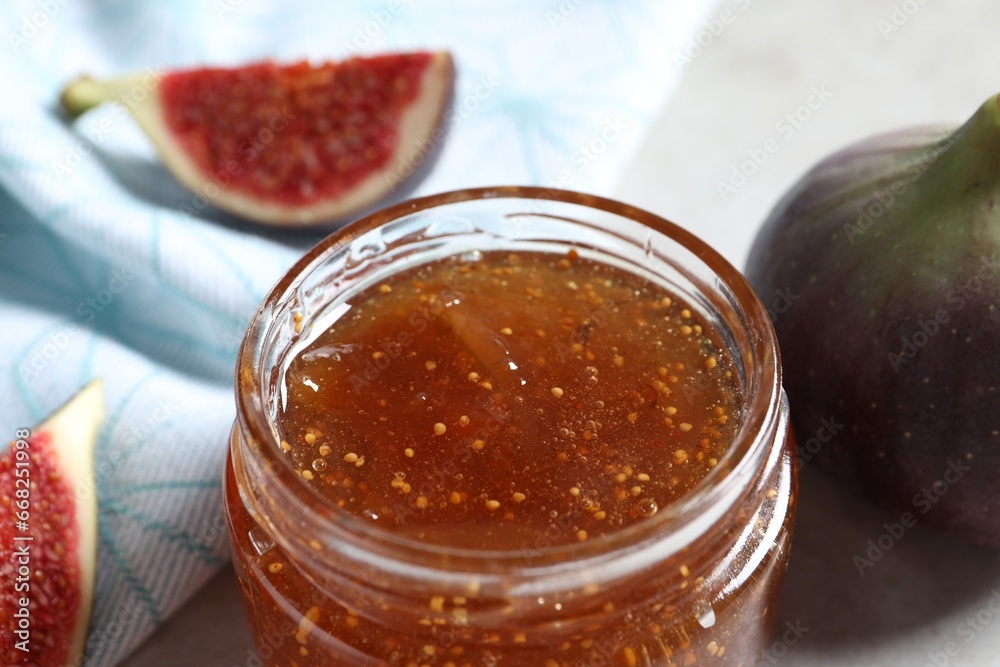 Jar of tasty sweet jam and fresh figs on table, closeup