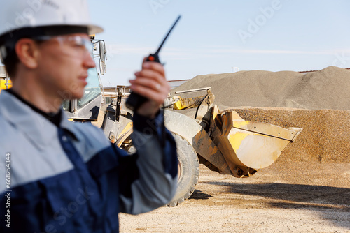 Concept open pit mine industry. Industrial worker of sand quarry use radio walkie talkie background yellow excavator working