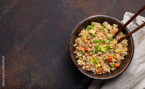 Authentic Chinese and Asian fried rice with egg and vegetables in ceramic brown bowl top view on dark rustic concrete table background. Traditional dish of China, space for text