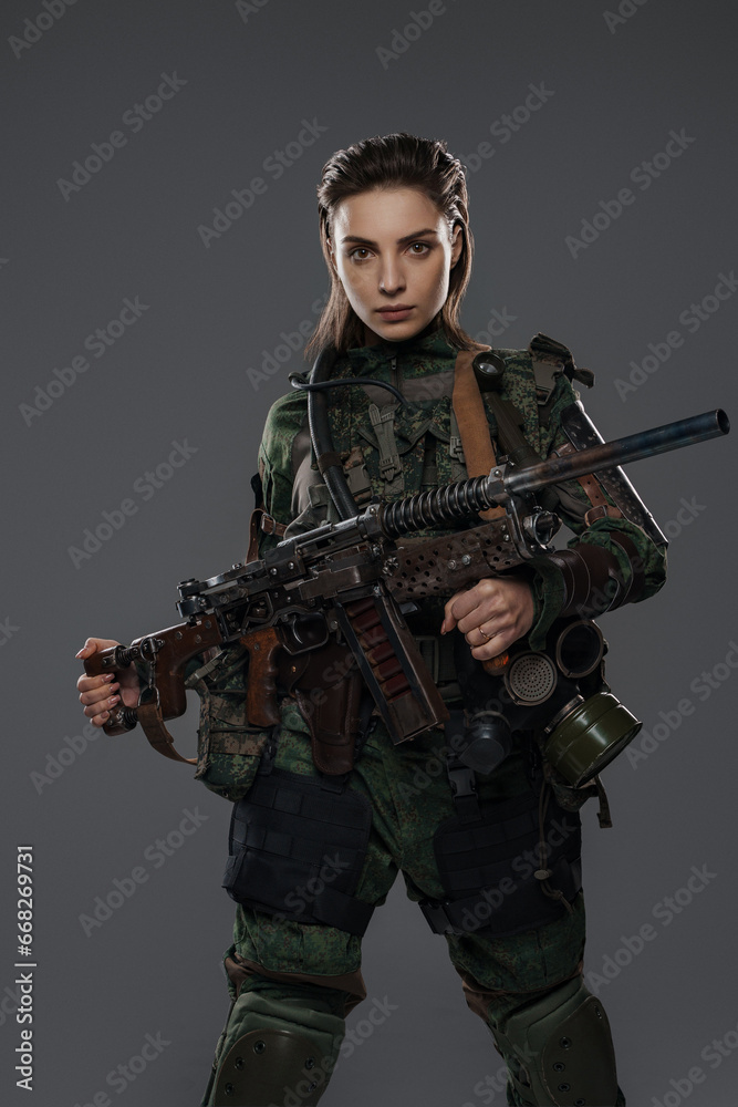 Portrait of a female soldier in military attire, holding a homemade automatic rifle, depicting a rebel or partisan in a Middle Eastern conflict against a gray background Portrait of a female soldier in military attire, holding a homemade automatic rifle, depicting a rebel or partisan in a Middle Eastern conflict against a gray background