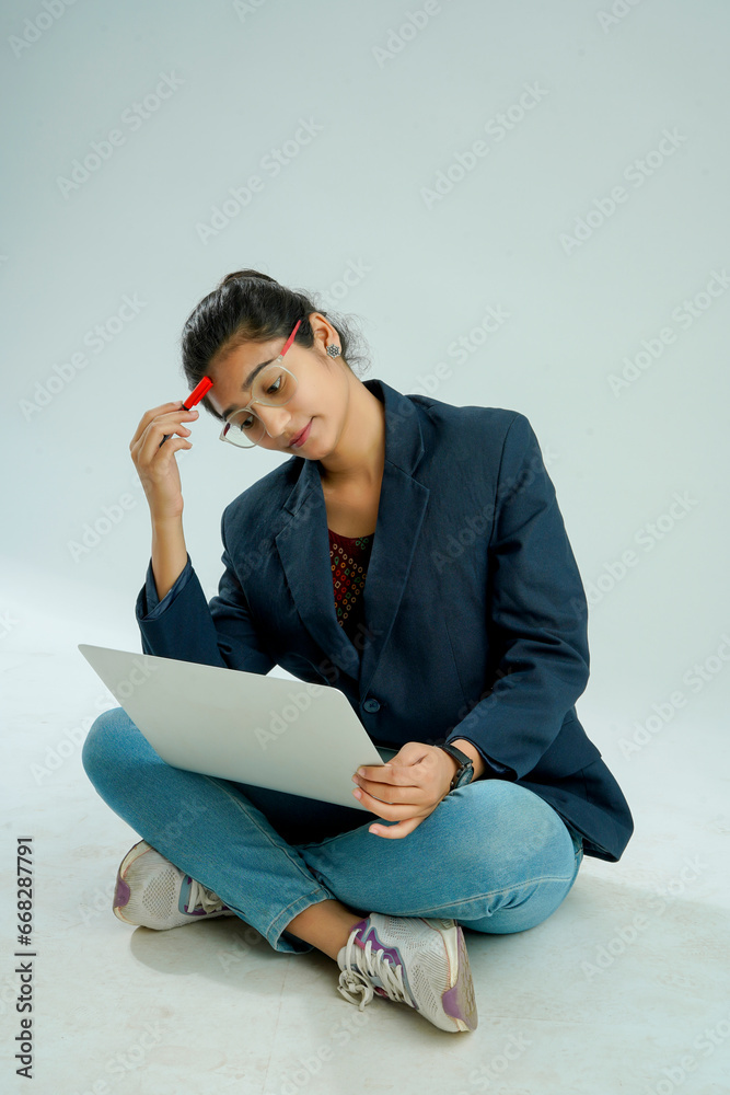 indian girl seated on a white background balances a laptop on her lap indian girl seated on a white background balances a laptop on her lap