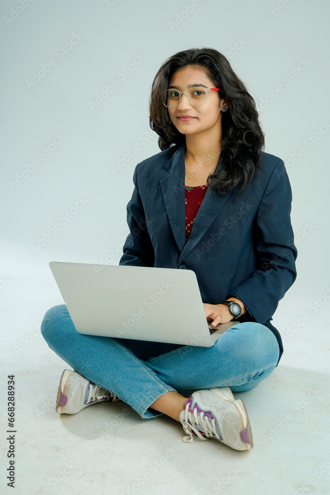 indian girl seated on a white background balances a laptop on her lap indian girl seated on a white background balances a laptop on her lap