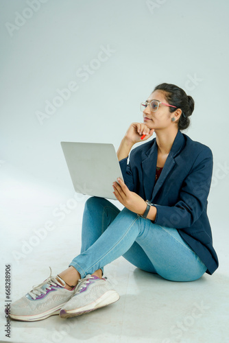 indian girl seated on a white background balances a laptop on her lap