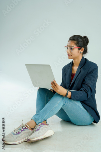 indian girl seated on a white background balances a laptop on her lap